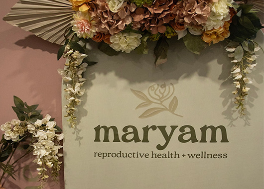 A large bouquet of flowers draped over a sign reading "maryam reproductive health and wellness"